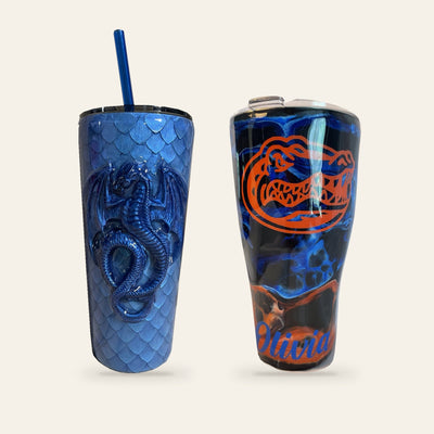 Marilu's actual handmade blue dragon scales tumbler and blue-and-orange Gators Olivia tumbler, photographed and arranged on ivory.
